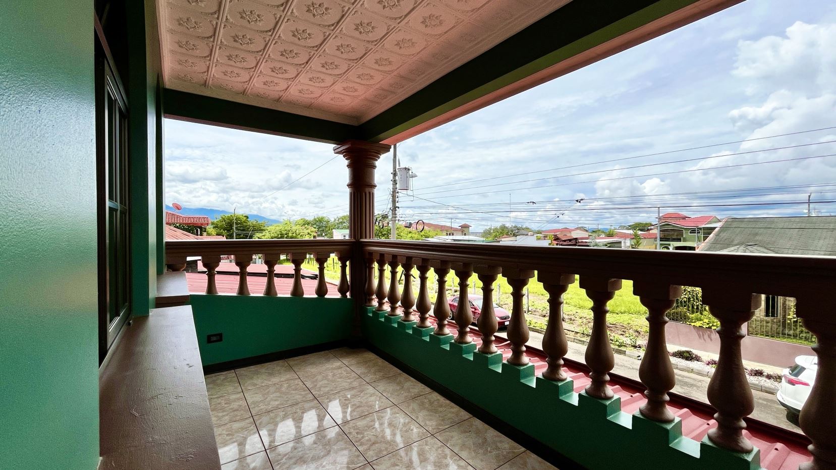 Green-painted balcony with brown decorative balusters and tiled floor, overlooking a suburban street.
