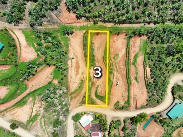 Aerial view of a rural construction site with a rectangular plot outlined in yellow and labeled '3' amid red soil and green vegetation on winding dirt roads