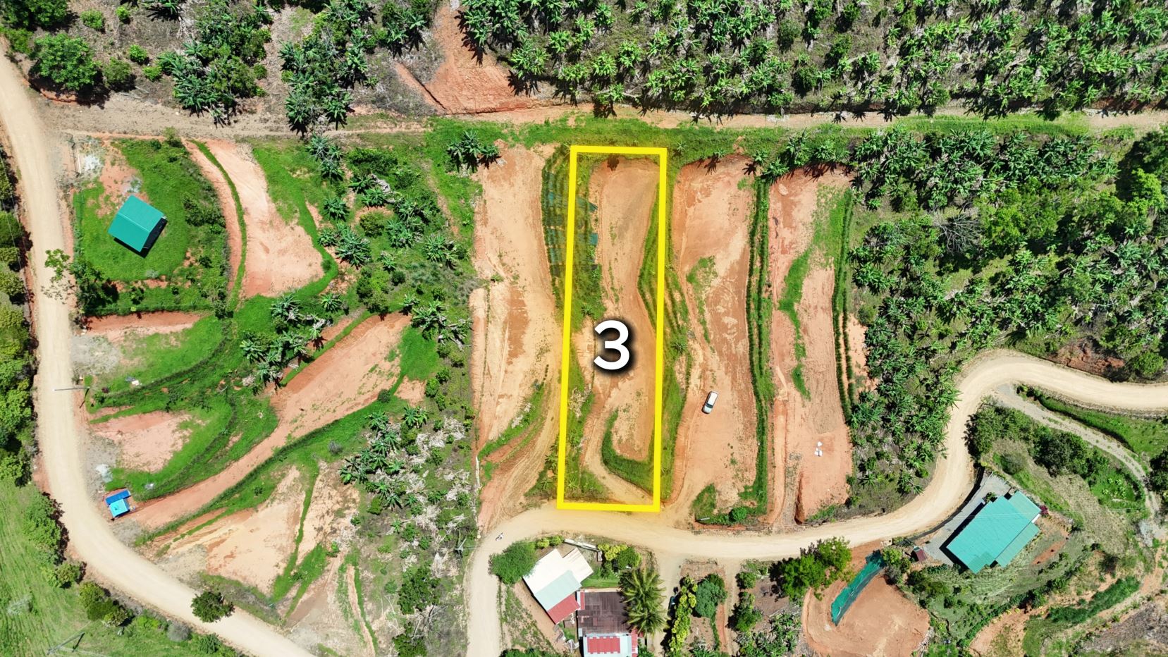 Aerial view of a rural construction site with a rectangular plot outlined in yellow and labeled '3' amid red soil and green vegetation on winding dirt roads