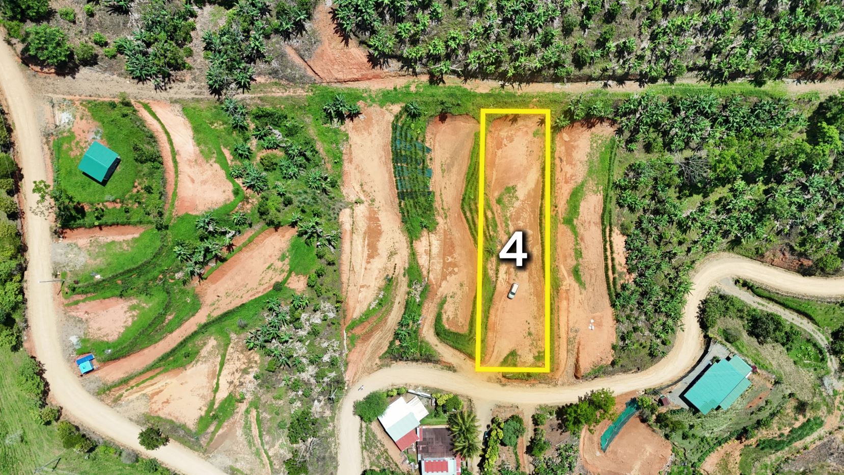 Aerial view of a rural site with plot 4 outlined in yellow along a dirt road and surrounding trees.