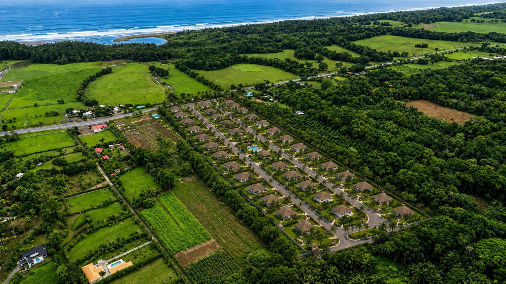 Aerial view of a coastal resort town with rows of houses, palm trees, and green fields by the ocean.