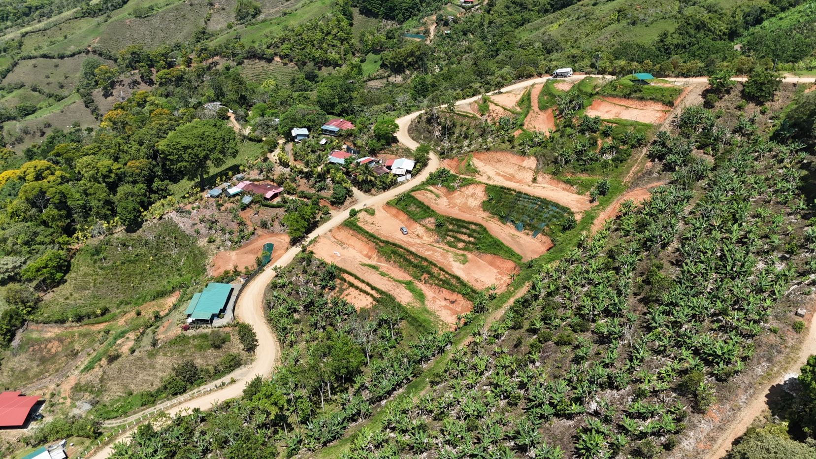 Aerial view of terraced farmland on a hillside with small village houses and palm trees nearby.