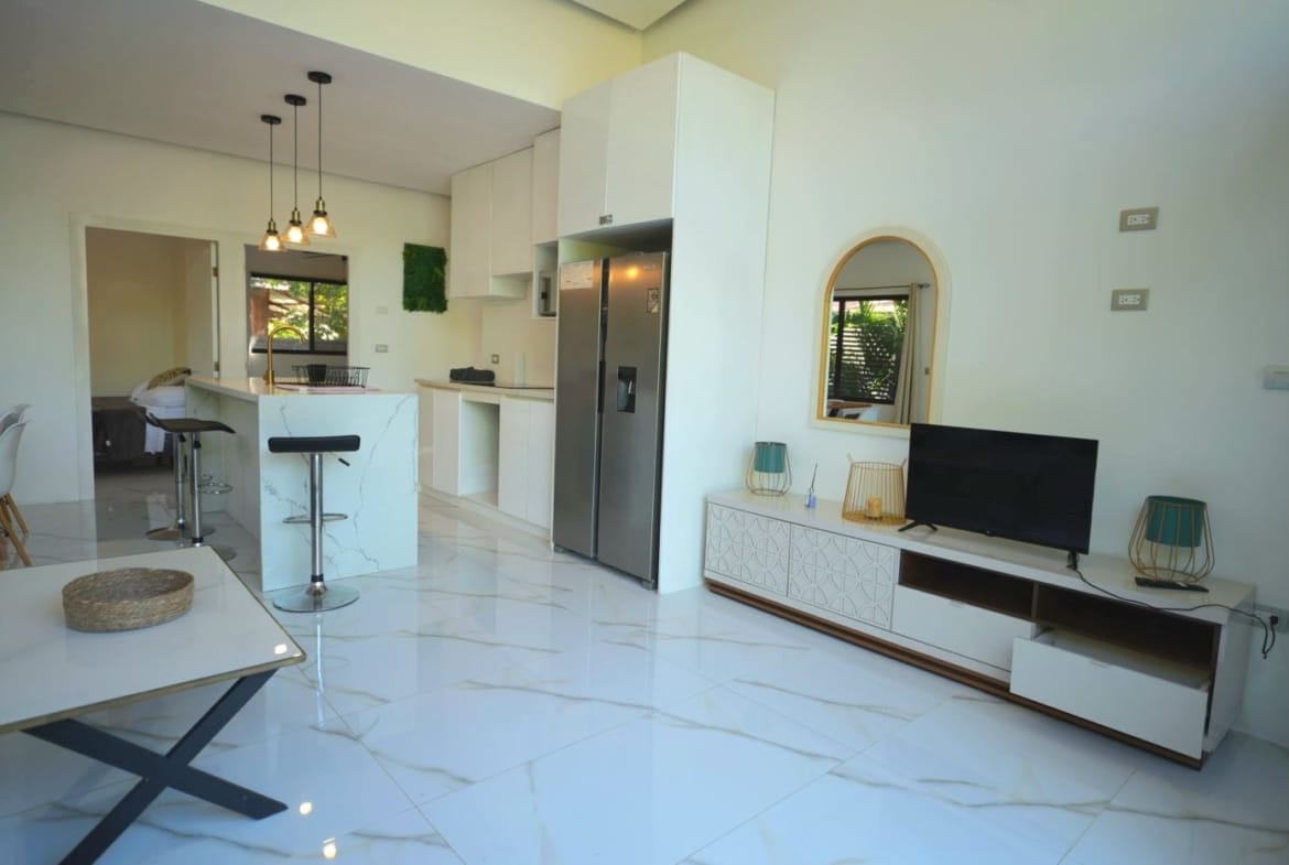 Open-plan living area with white marble floors, a marble-topped kitchen island, bar stools, and a stainless steel fridge.