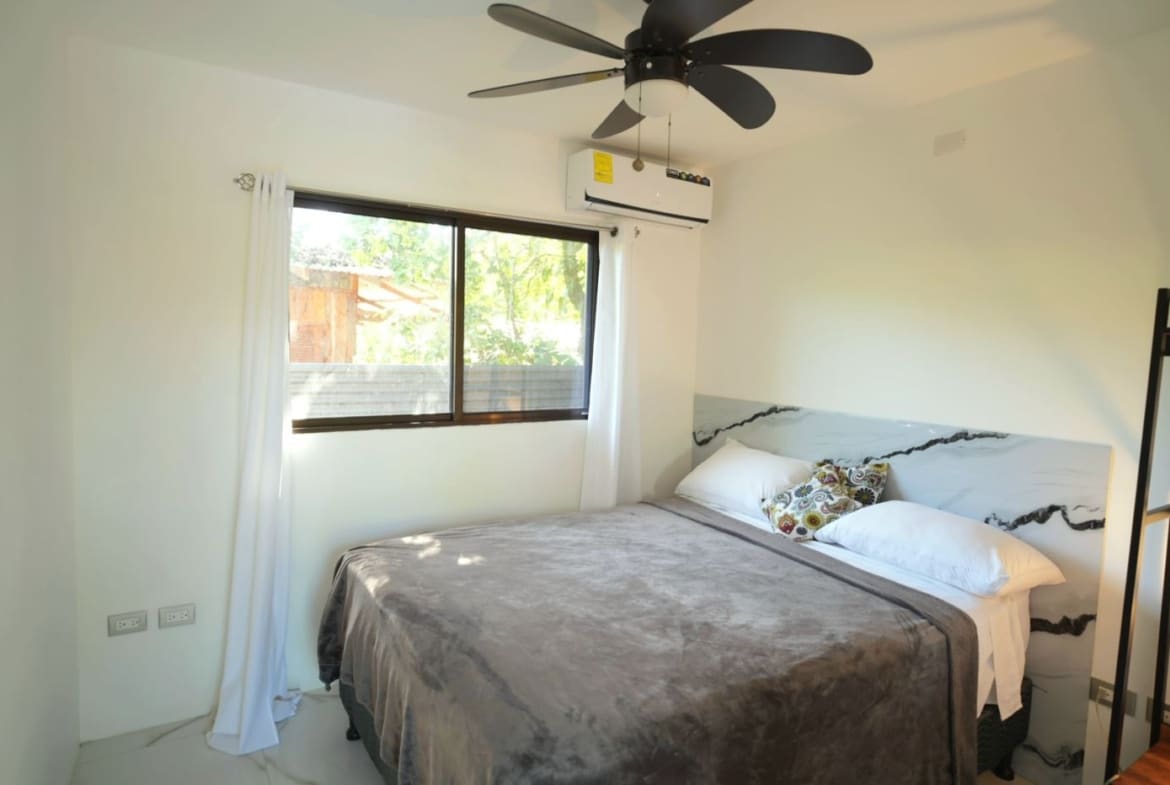 Bright bedroom with a large bed, gray blanket, white pillows, and a marble-veined headboard near a window.