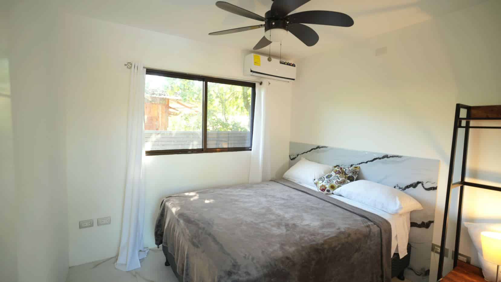 Bright bedroom with a large bed, gray blanket, white pillows, and a marble-veined headboard near a window.