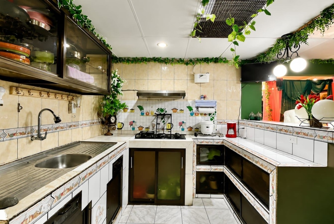 U-shaped kitchen with tiled counters, sink, stove, and hanging greenery along the ceiling.