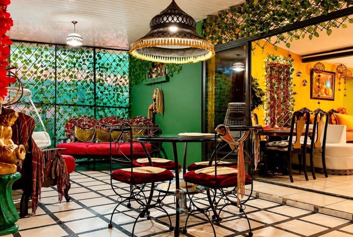Colorful indoor dining area with a glass table and ornate red-cushioned chairs under a decorative hanging lamp