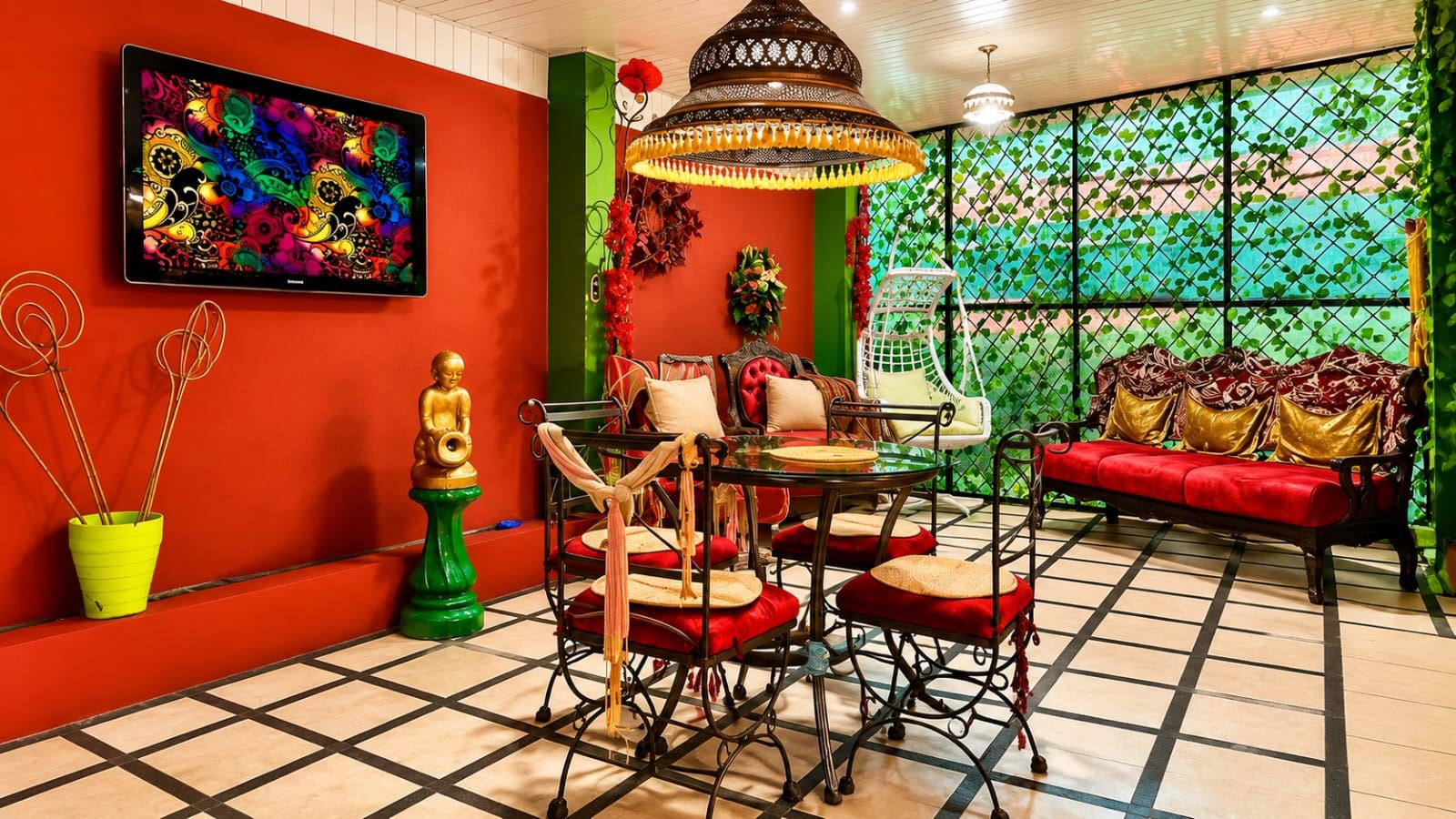 Vibrant indoor lounge with red walls, wrought-iron furniture, red cushions, and a colorful wall TV art piece on the left.