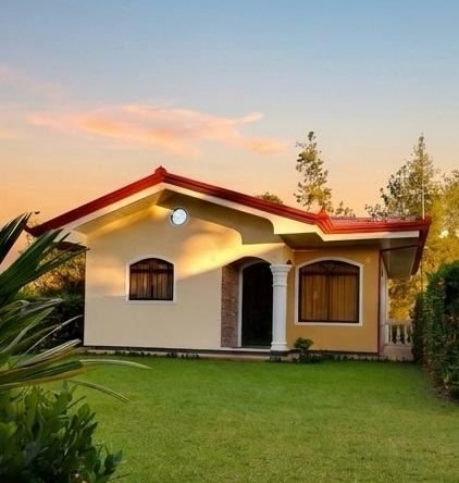 Single-story yellow house with a red roof and white columns, arched windows, on a green lawn at sunset.