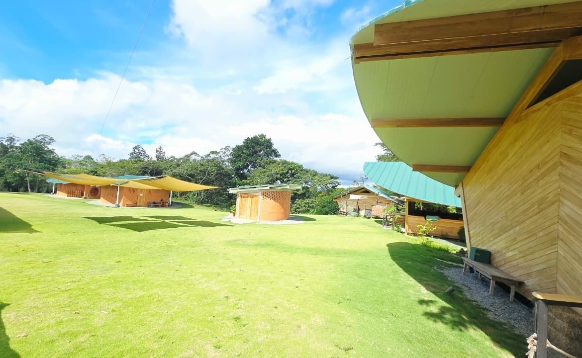 Open grassy campsite with tan brick huts and large yellow shade sails under a bright blue sky. Note: concise and informative for context as a campsite image.