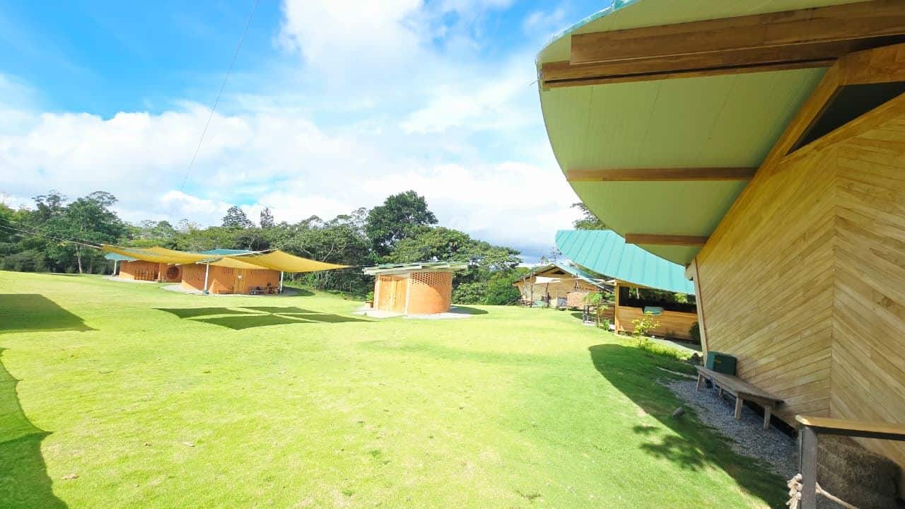 Open grassy campsite with tan brick huts and large yellow shade sails under a bright blue sky. Note: concise and informative for context as a campsite image.
