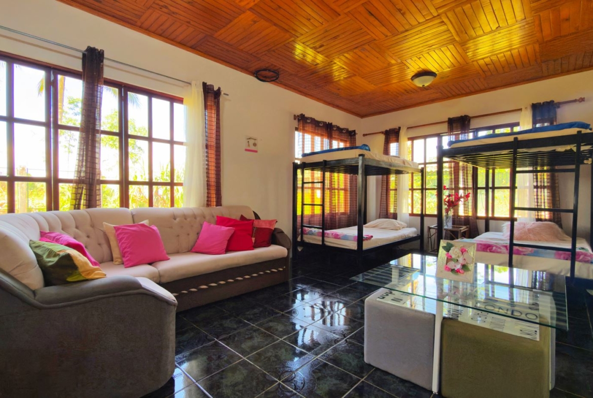 Bright living room with a cream tufted sofa, colorful cushions, two bunk beds, and large windows showing greenery.