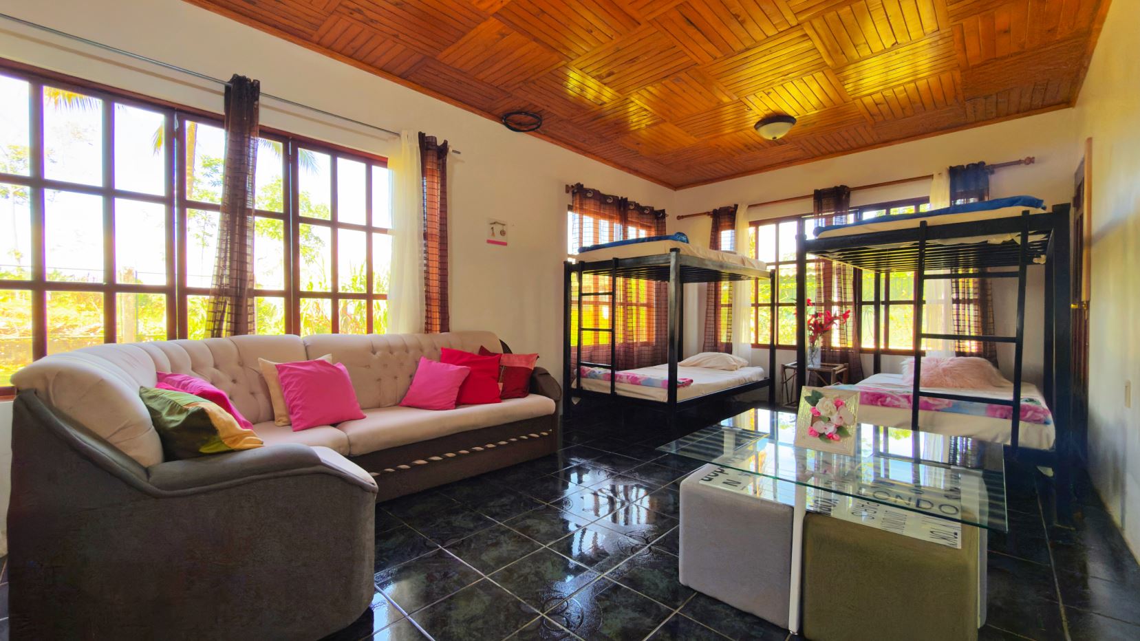 Bright living room with a cream tufted sofa, colorful cushions, two bunk beds, and large windows showing greenery.