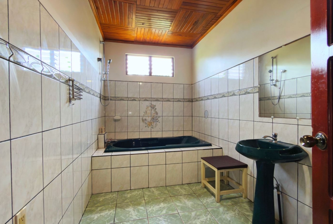 Bathroom with white tiled walls, a green built-in tub, a matching green pedestal sink, and a wooden ceiling; doorway visible on the right side.