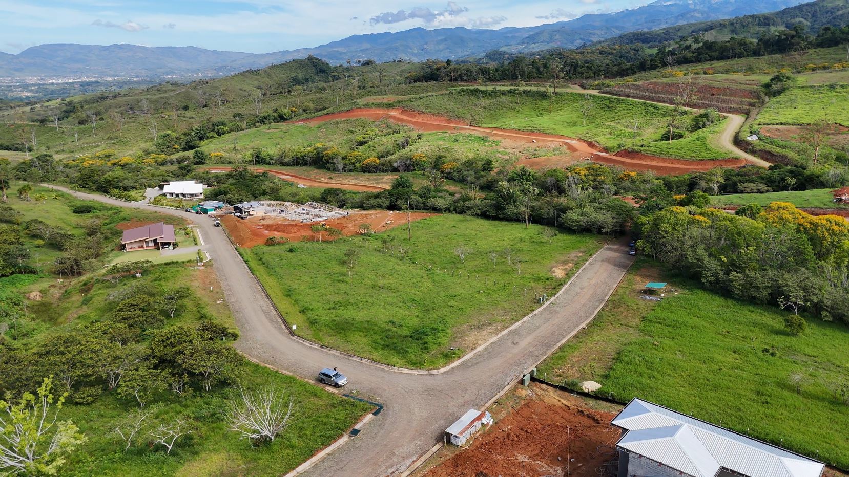 Aerial view of a rural construction site on rolling hills, with red dirt roads and green fields in the landscape.