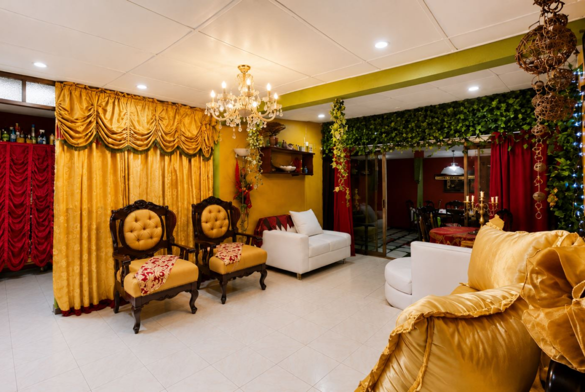 Luxurious living room with gold curtains, a crystal chandelier, and tufted upholstered chairs surrounding a seating area.