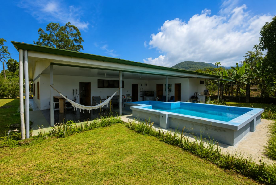 White, single-story home with a covered patio and hammock overlooking a rectangular blue pool in a grassy yard.