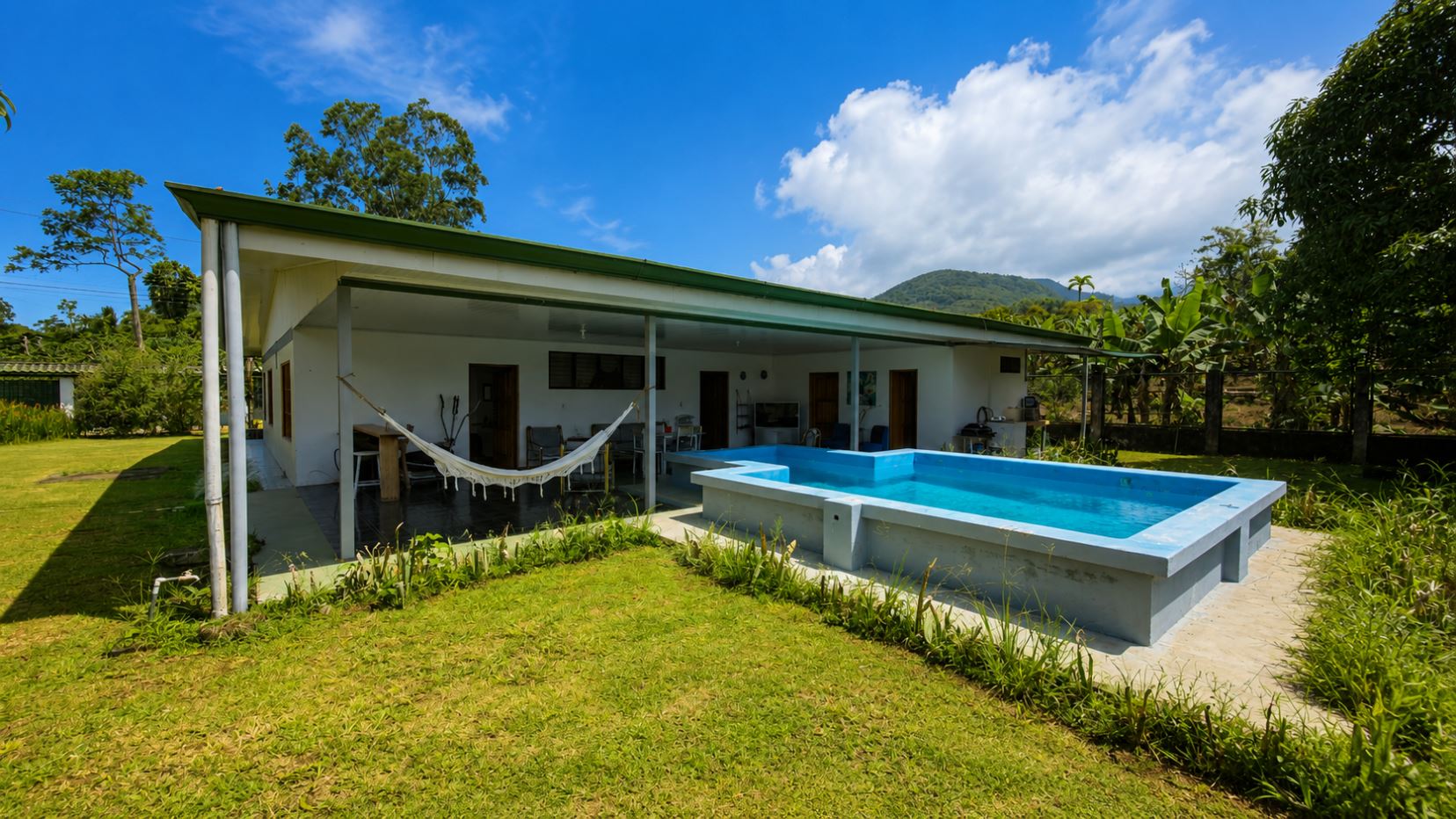 White, single-story home with a covered patio and hammock overlooking a rectangular blue pool in a grassy yard.