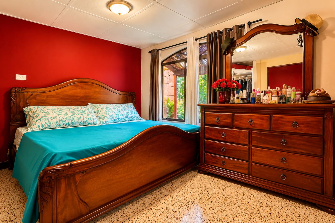 Wooden king-size bed with teal bedspread and patterned pillows, red accent wall behind.