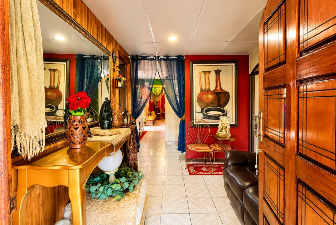 Luxurious hallway leading to a living room, with red walls, blue sheer curtains, a gold console table, and a vase of red roses.
