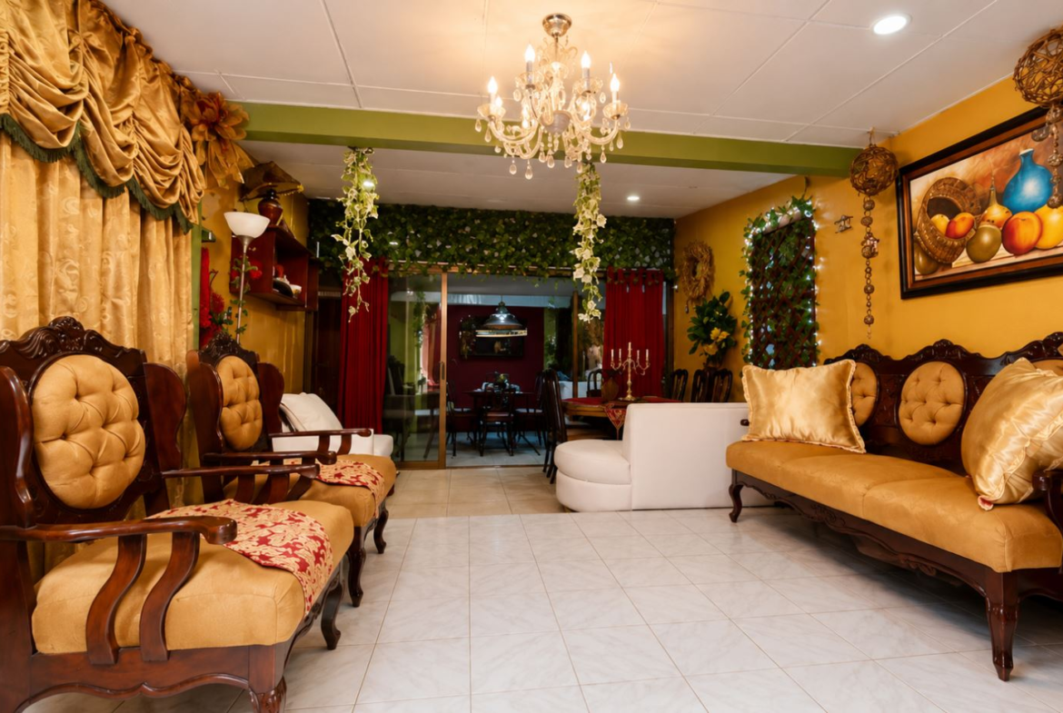Elegant gold-toned lounge with tufted wooden chairs, matching sofa, and lush drapes under a chandelier.