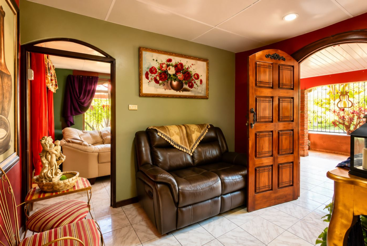 Cozy living room with a green wall, brown leather loveseat, and a fringed throw, above which hangs a framed flower painting.