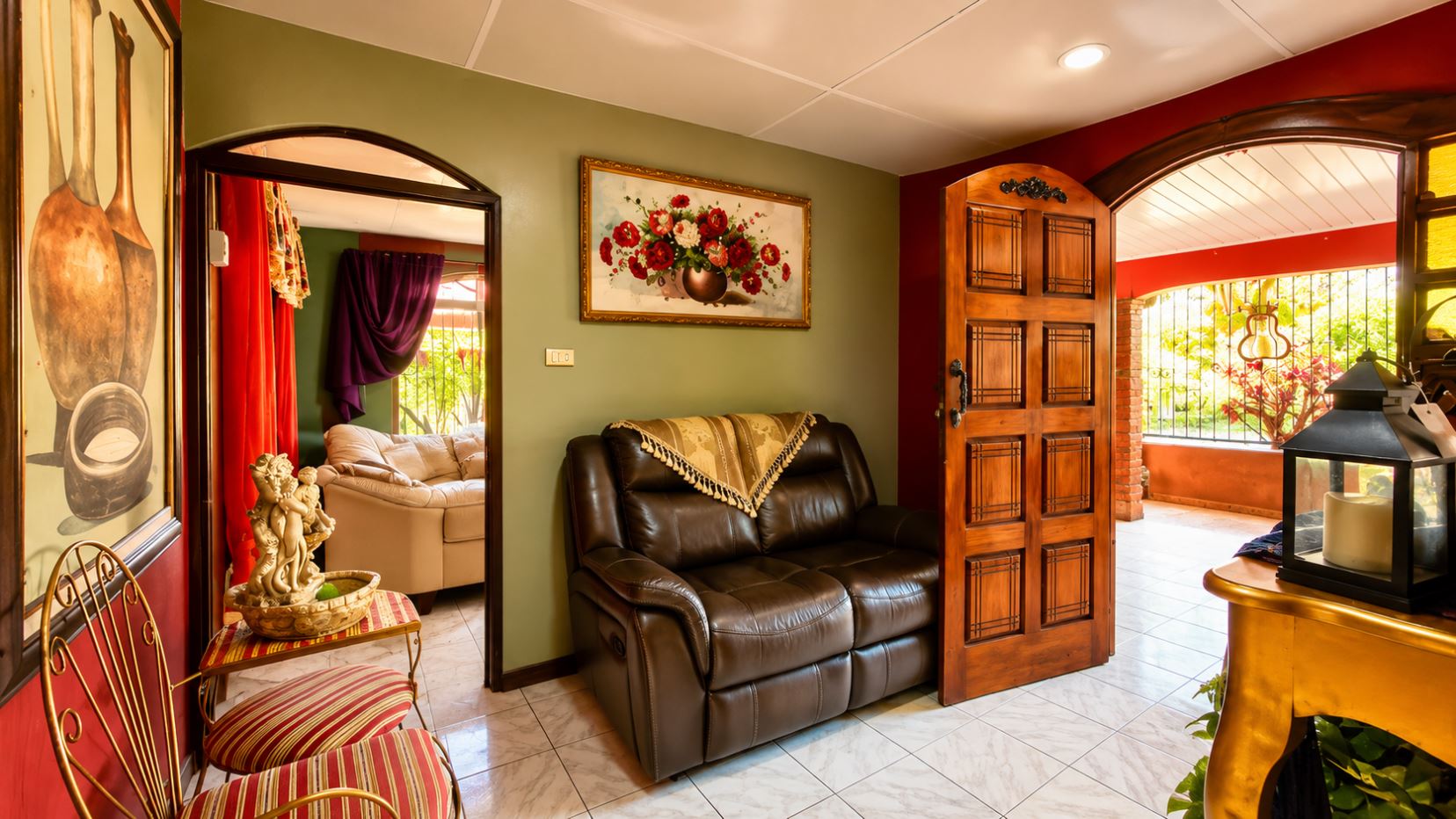 Cozy living room with a green wall, brown leather loveseat, and a fringed throw, above which hangs a framed flower painting.